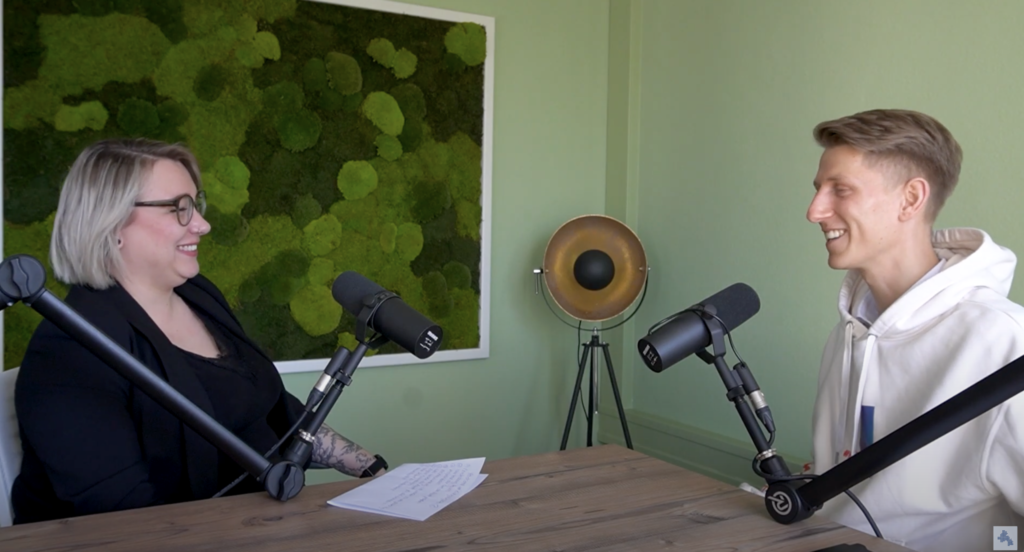 Podcast Erfolgsbegleiter: Zwei Personen am Tisch mit Mikrofonen. Azubis und Fachkräfte im Gespräch.